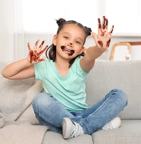 Kleines Mädchen mit verschmierten Händen auf einem hellen Sofa