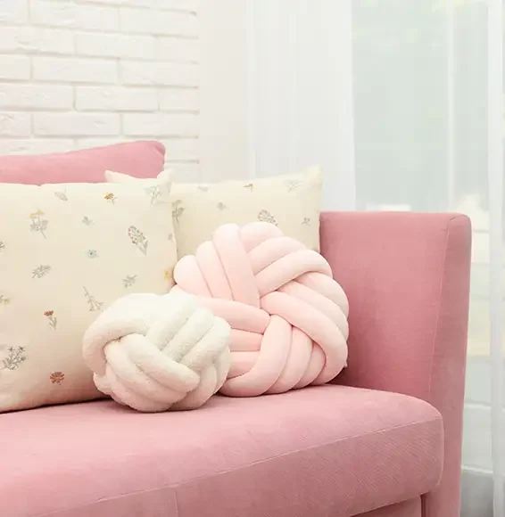 Eine himbeerfarbene Couch mit Baumwollkissen in Rosé und Crème